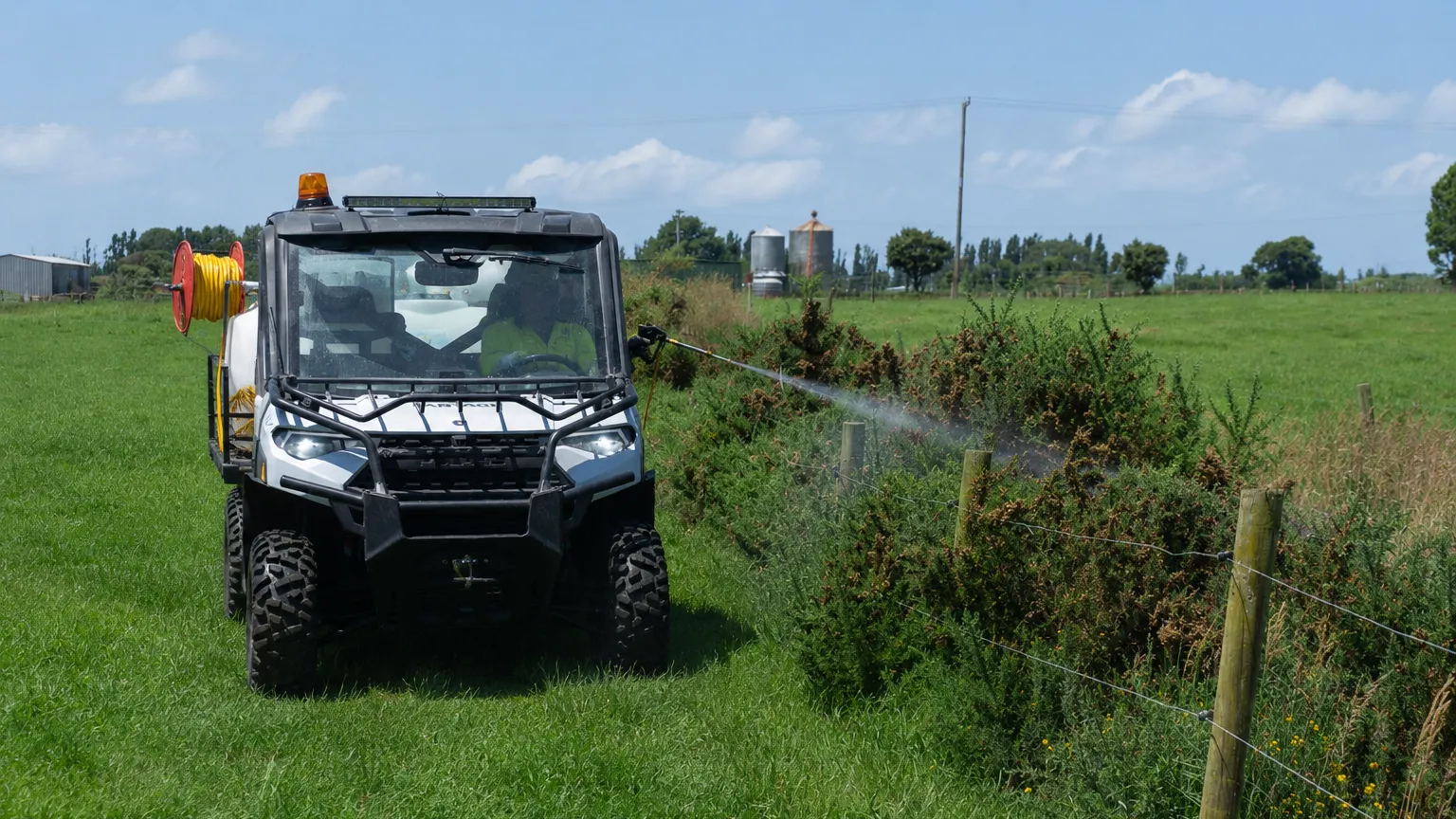A Polaris ground rig with hose and reel spraying along a farm fence line