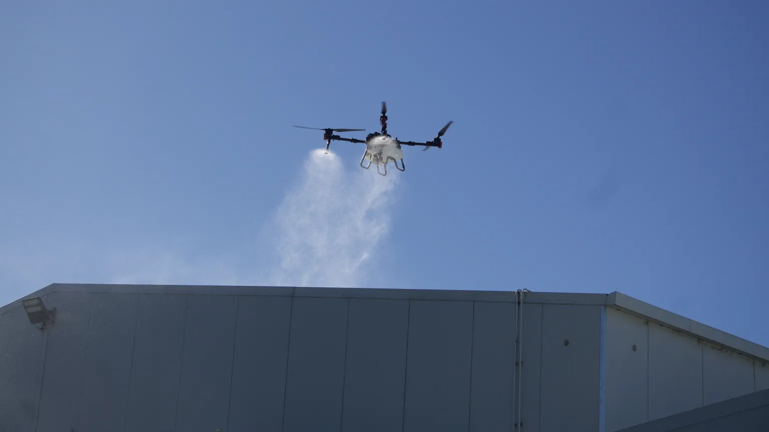 A drone applying moss and mould treatment across a large commercial roof