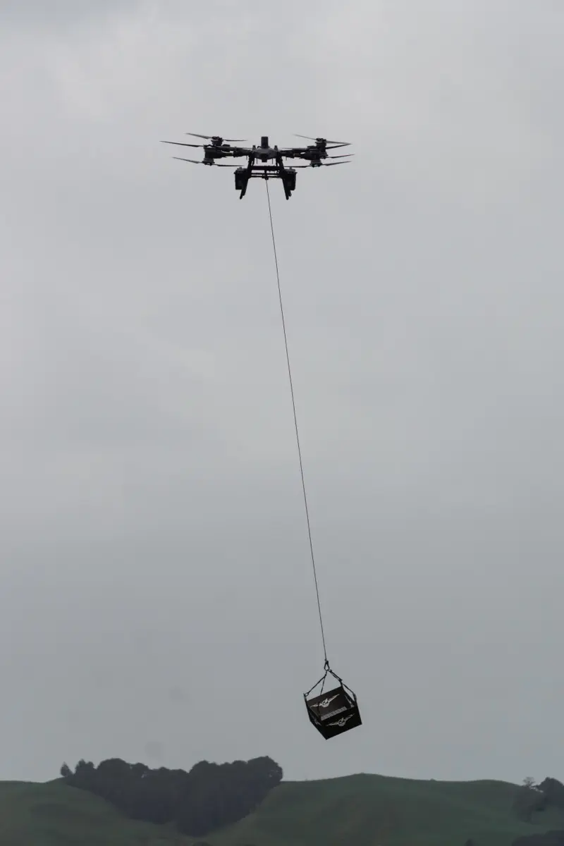 A lifting crate on a long line under the drone over farmland