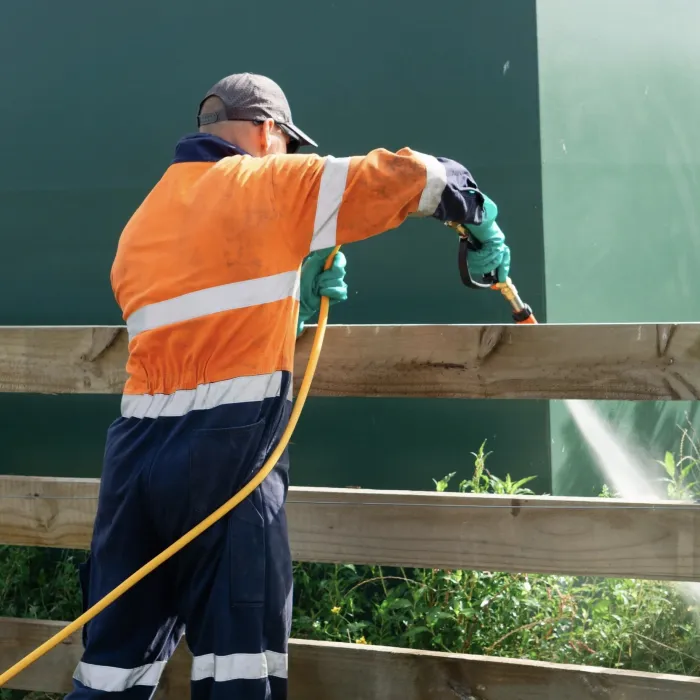 A worker in hi-vis hand-spraying treatment along a fence and wall