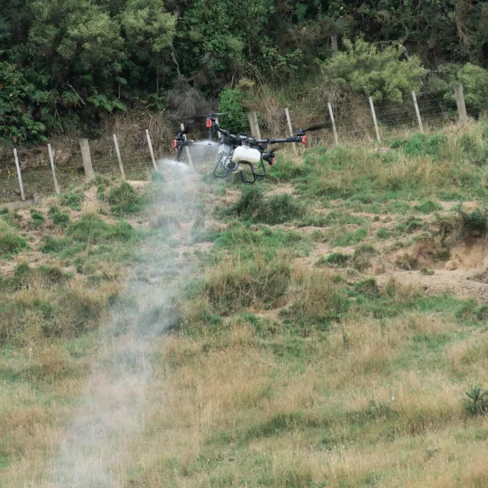 A spray drone treating weeds down a steep gully and fence line