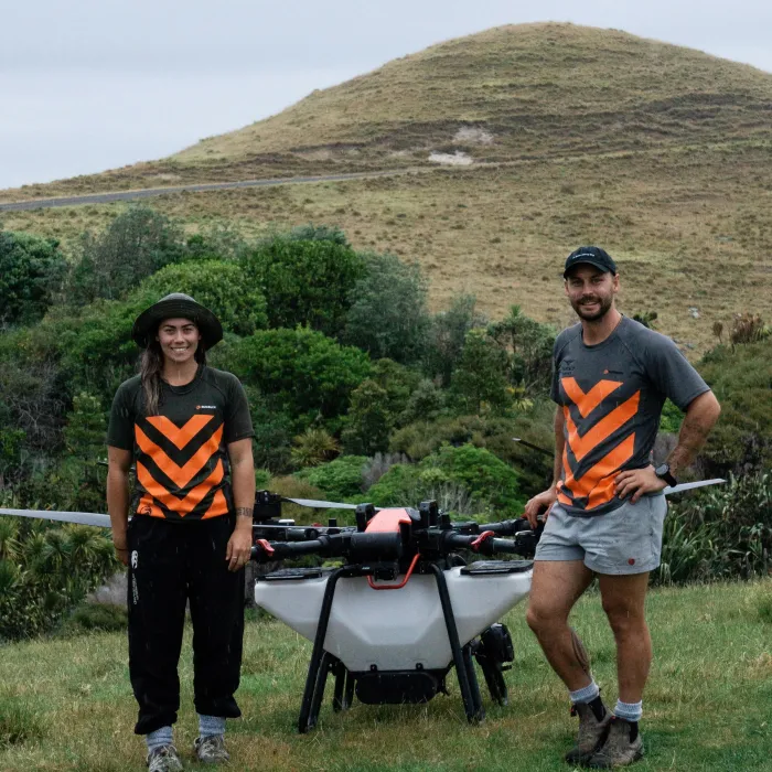 Two Vantage Drone Services operators standing beside a large spray drone in hill country