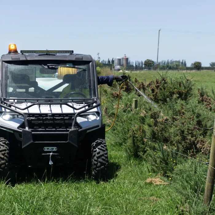 An operator hand-spraying a fence line from the Polaris side-by-side